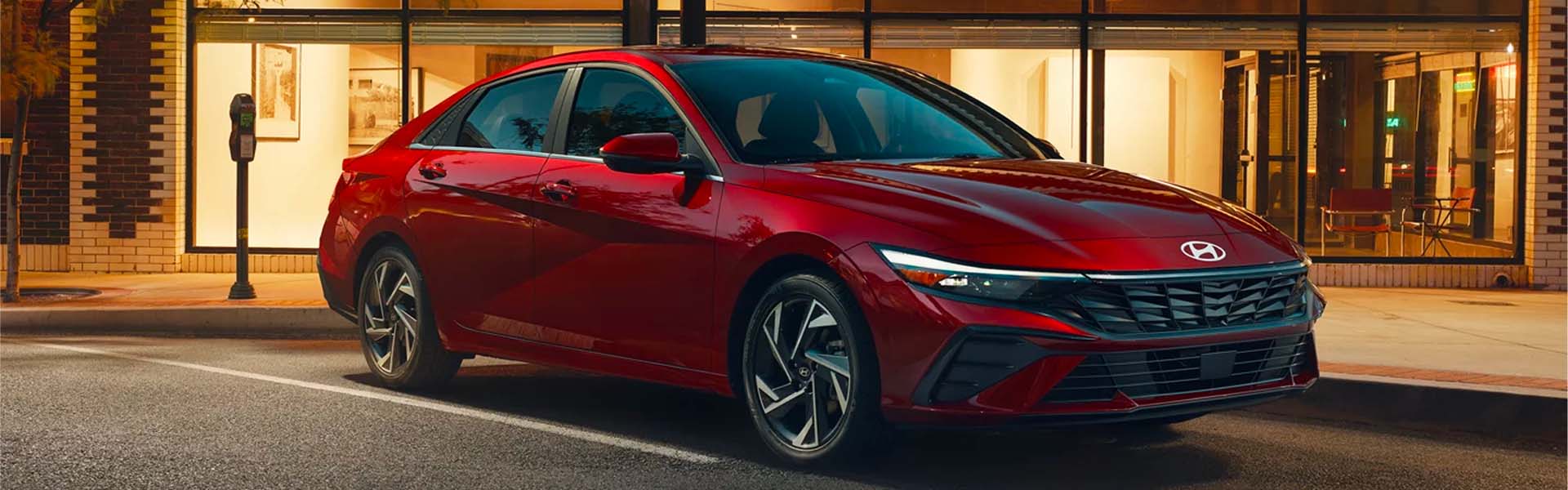 A sleek red Hyundai Elantra parked on a city street at sunset.