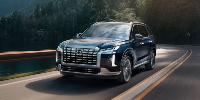Front three-quarter view of a blue Hyundai Palisade driving on a road.