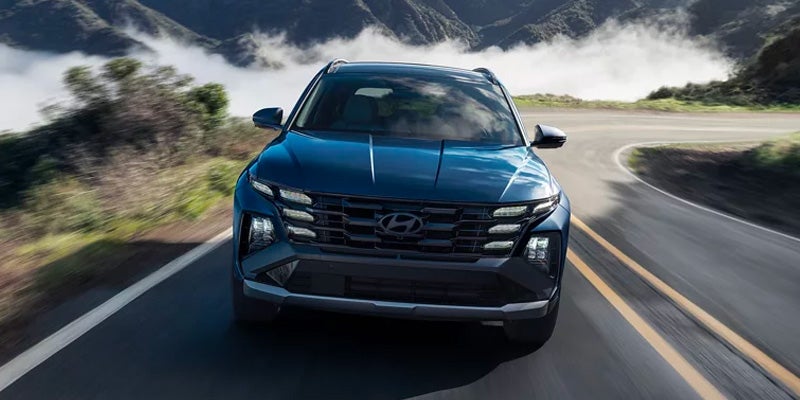 Front view of a blue Hyundai SUV driving on a winding road.