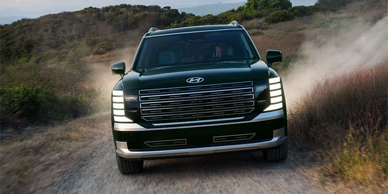 Front view of a dark green SUV driving on a dirt road.