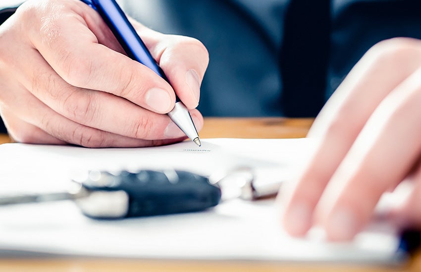 A close-up of a person signing paperwork with a car key nearby